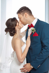 Young wedding couple kissing against a window