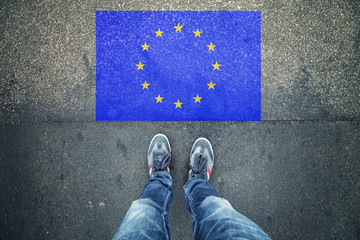Point of view of a person legs standing in front of EU Flag painted on city asphalt street ground.