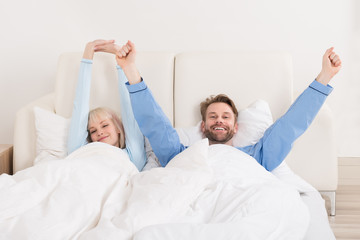 Happy Couple Raising Hands On Bed