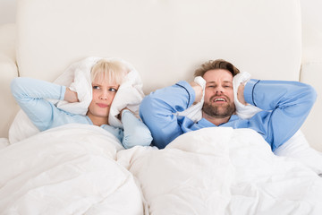 Couple Covering Ears While Sleeping On Bed