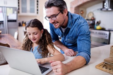 Father and daughter using laptop in kitchen