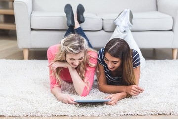 Two beautiful women lying on rug and using digital tablet