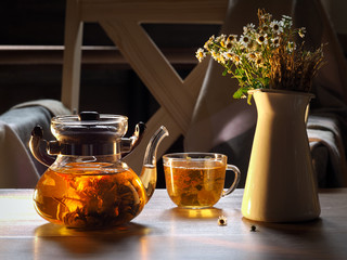 Green tea is brewed in a transparent teapot. Tea leaves in the form of a flower. On the table with...