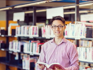 Happy male student holding books at the library