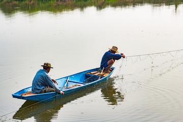 The fisherman in the boat use net to catch fish in the river.