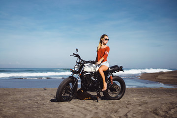 Fototapeta na wymiar young pretty hipster girl Biker girl sitting on vintage custom motorcycle Biker girl sitting Outdoor lifestyle portrait. jeans short denim, fashion style