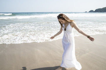 Fototapeta na wymiar Woman wearing a white long dress is walking the beach