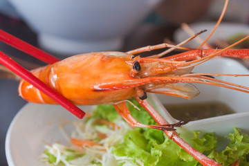 Red chopsticks holding a prawn.