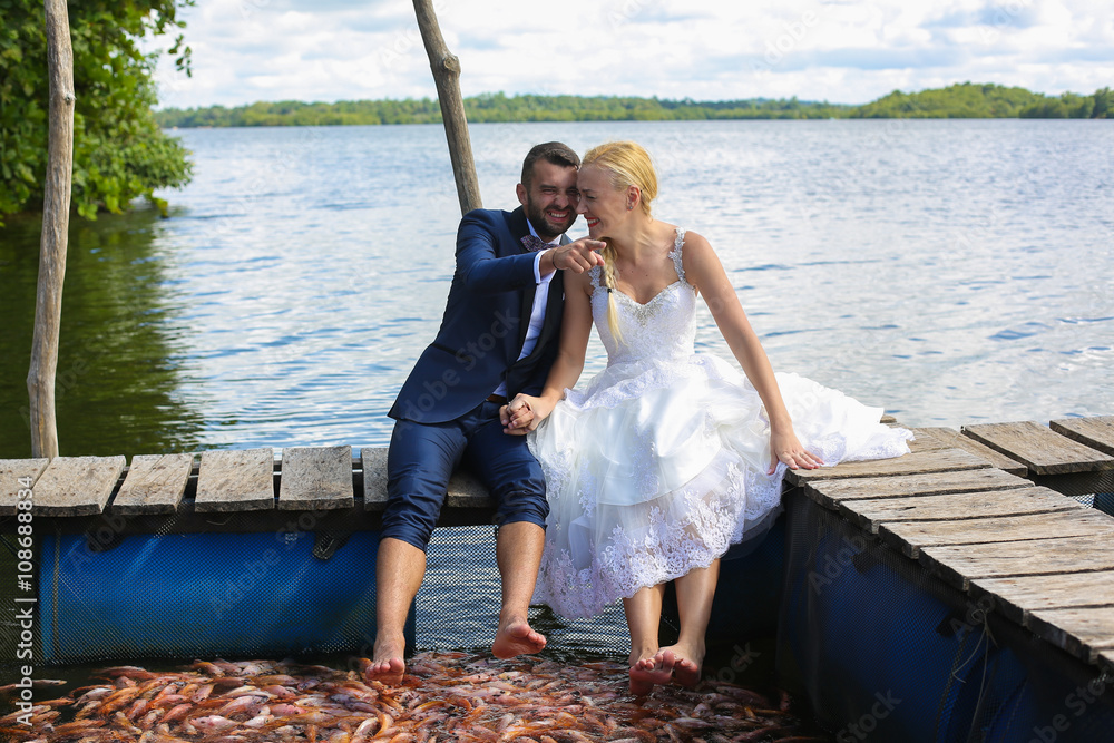 Wall mural bride and groom sitting with their feet in water