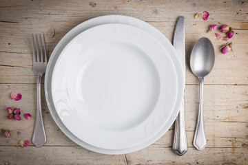 Dinner place setting - fork, knife, spoon, two plates with small dried rosebud