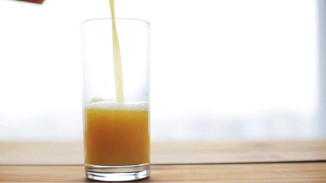 orange juice pouring into glass on wooden table