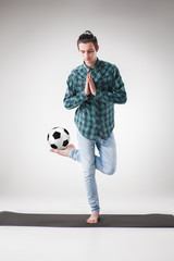 Portrait  of young man, practicing yoga with football ball