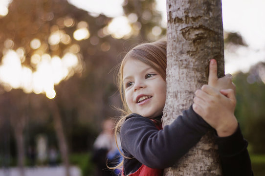 Beautiful little girl smiling, hugging a tree trunk. Little girl