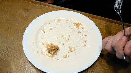Piece of creamy sweet cake being cut with fork on white plate and eaten in a cafe restaurant. Close up shot. 