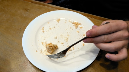 Piece of creamy sweet cake being cut with fork on white plate and eaten in a cafe restaurant. Close up shot. 