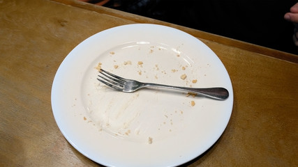 Person finished to eat and put fork on the empty plate. Cafe restaurant casual scene. 