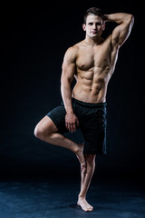 Young strong athlete is making yoga on black background