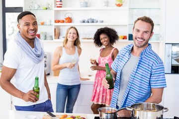 Friends holding beer bottles and glasses of wine in kitchen