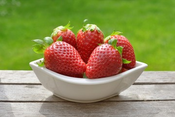 Red strawberry in a bowl, on old wood.