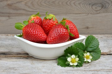 Red strawberry in a bowl, on old wood.