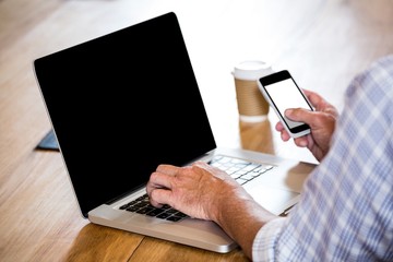 Man text messaging on phone while using a laptop