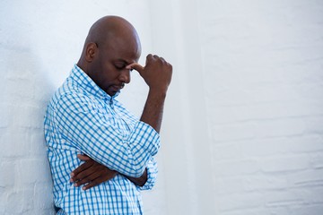 Upset man with eyes closed leaning against a wall 