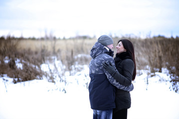 Happy young couple hugging outdoors in a snowy park. Love hugs, family relationships