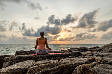 Fototapeta na wymiar Young woman practices yoga on the rocks against the sea 