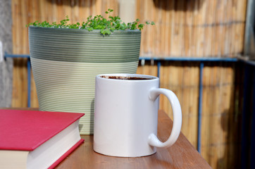 Red book, cup of coffee and green plant in flowerpot on small balcony table