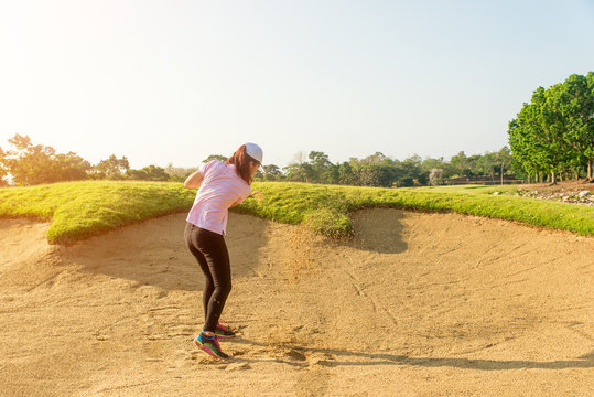 Asain woman golfer hitting golf ball out of a sand trap