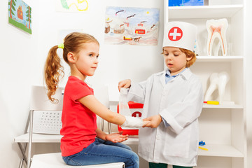 Little pediatrician doctor bandaging girl's arm