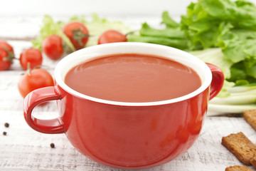 Tomato soup in red ceramic bowl on rustic wooden background.