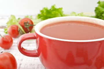 Tomato soup in red ceramic bowl on rustic wooden background. 