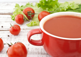 Tomato soup in red ceramic bowl on rustic wooden background. 