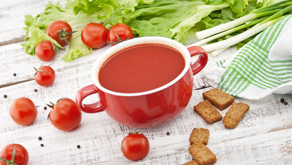 Tomato soup in red ceramic bowl on rustic wooden background. 