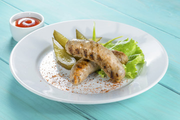 Grilled chicken sausages with pickles on a wooden background