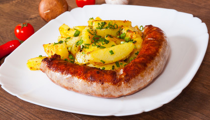 grilled meat sausages with fried potatoes in a plate on wooden table