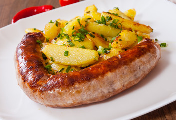 grilled meat sausages with fried potatoes in a plate on wooden table