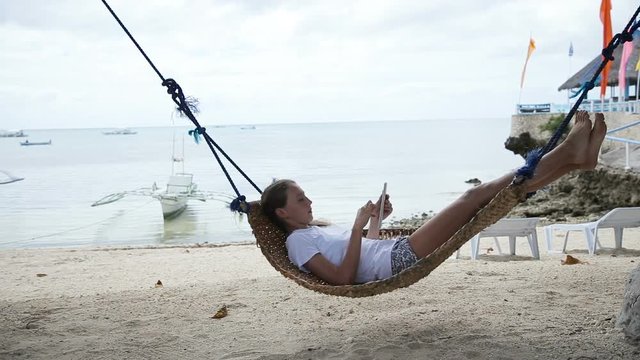 Young girl relaxing on hammock and using digital tablet.girl lies in a hammock on a tropical beach and playing with a digital tablet.Travel concept.Family,summer vacation.Happy family