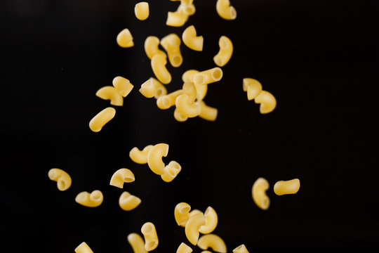 Falling gobetti pasta. Flying yellow raw macaroni over black background. 
