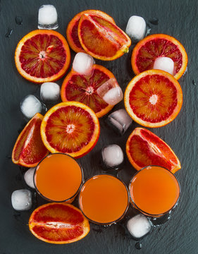 Sliced Sicilian red oranges and orange juice in small glasses on black stone background. Top view.