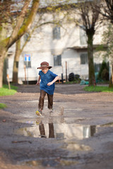 Fototapeta premium Little boy splashing in a mud puddle, jumping into a puddle 