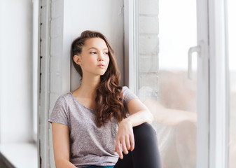 sad pretty teenage girl sitting on windowsill