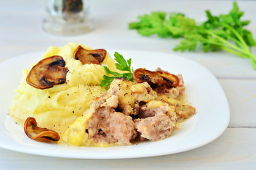 Mashed potatoes with meat and mushrooms on a white plate. Parsley in the background
