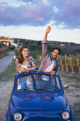 Young couple doing a road trip in Tuscany countryside in a vintage car