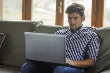 Very focused young man wearing plaid shirt sitting on the couch