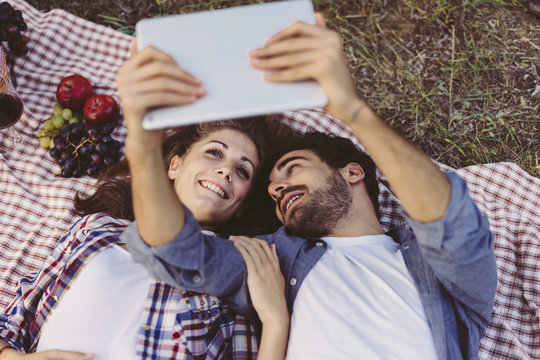 Young couple in love doing a picnic outdoors and using a tablet