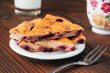Cake with currants, fork, glass of milk and a cup on a brown tab
