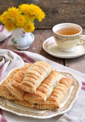 Pies of puff pastry with a cup of tea on a wooden table. Vintage style.