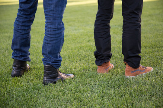Legs of two men with blue jeans and black trousers on a Green Meadow